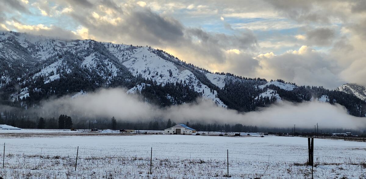 Fog lifting off snow-covered mountains above a ranch in winter